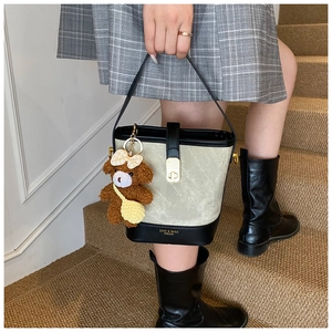 Detail of grey fabric bucket bag with black leather trim, gold lock and plush bear charm