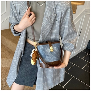 Detail showing denim blue fabric bucket bag with brown leather trim and bear pendant