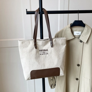 Dettaglio della borsa tote in velluto a coste crema con manici in pelle marrone e scritte