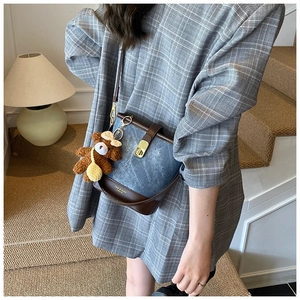Detail of vintage denim bucket bag with brown leather trim and cute plush bear charm