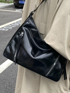 Large black glossy tote bag with silver zipper detail, worn as a shoulder bag by model