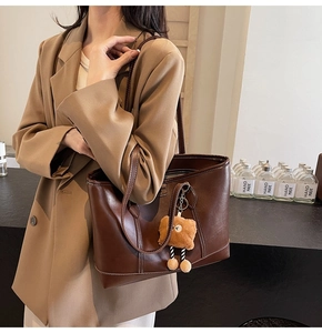 Détail d'un sac cabas en cuir marron avec surpiqûres blanches et pendentif ours peluche