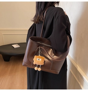 Détail d'un sac cabas marron vintage avec coutures contrastées et breloque monstre en peluche