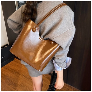Detail van glanzende bruine leren shopper met unieke bolvormige hardware op het model