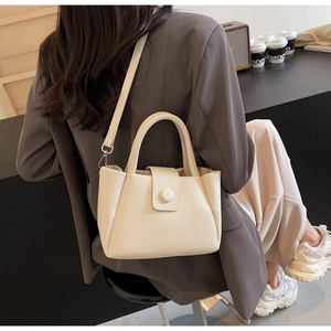 Detail of cream-colored pebble leather texture and crossbody strap on the bucket bag