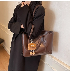 Détail du cabas en cuir marron avec surpiqûres contrastées et breloque poupée en peluche