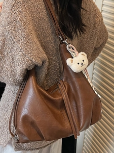 Brown vintage large tote bag with plush bear charm shown in a crossbody style