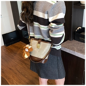 Detail view of canvas and leather bucket bag with a plush bear charm on a female model