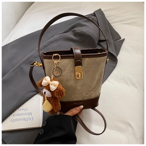 Detail of canvas bucket bag featuring a brown teddy bear charm and gold twist-lock