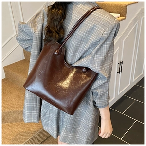 Detail van grote bruine tote bag van glanzend leer met ronde bolvormige accenten op het handvat
