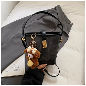 Detail of black bucket bag with gold clasp and cute plush bear charm on a suit fabric