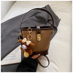 Detail view of brown bucket bag with gold clasp and a cute bear bag charm accessory