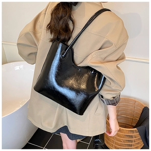 Modieuze zwarte glanzende tote bag gedragen over de schouder als een chique okseltas