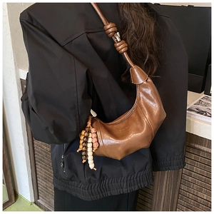 Détail du sac croissant en cuir marron avec bandoulière nouée et gland en perles de bois