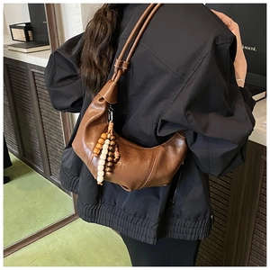 Vue détaillée d'un sac demi-lune en cuir marron avec un pendentif décoratif en perles