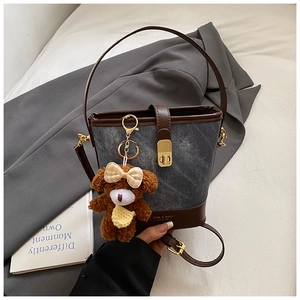 Detailed macro view of denim bucket bag with brown leather trim and metallic buckle closure