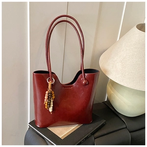 Detail van bordeauxrode leren tas met een golvende rand en gekleurde kralenhanger