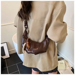 Détail d'un sac demi-lune marron foncé avec plis et perles décoratives en bois vintage