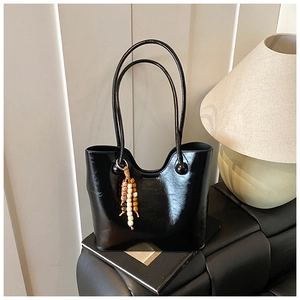 Detail van glanzende zwarte tote bag met lange hengsels en kralenhanger op een lederen bank