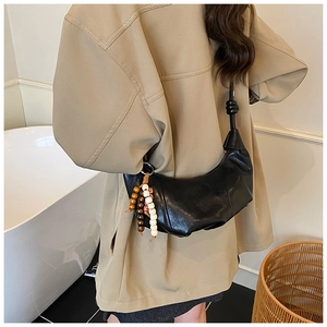 Détail d'un sac demi-lune noir avec pendentif en perles de bois et bandoulière à nœuds