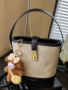 Chic beige canvas and black leather bucket bag with teddy bear charm on books