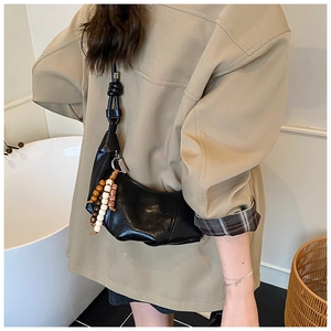 Détail du sac croissant noir avec texture cuir plissé et breloque perlée sur la bandoulière