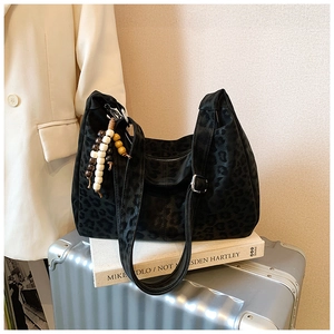 Detail of black leopard jacquard tote bag with wood bead charm on a travel suitcase