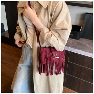 Détail d'un sac bandoulière en daim bordeaux avec franges et fermeture à boucle métallique