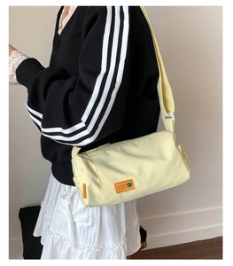 Detail of light yellow canvas crossbody bag with adjustable strap and orange brand tag