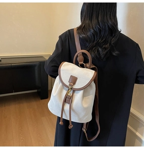 Close-up of white canvas backpack with brown leather straps and metal hook on model's back