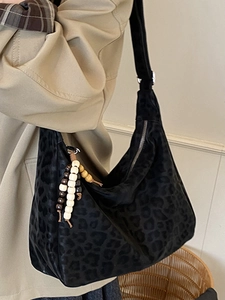 Large black leopard print hobo bag with wooden bead tassel shown on a shoulder