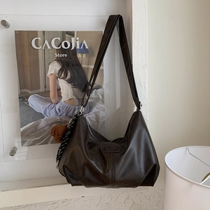 Detailed close-up of dark brown soft leather hobo bag with teddy bear charm and logo