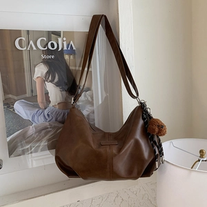 Detail of dark brown leather hobo bag featuring vertical stitching and a plush bear charm