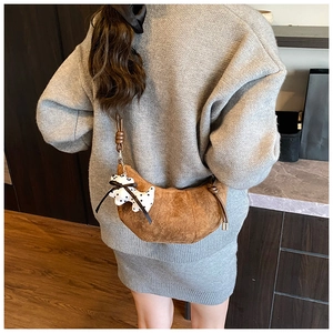 Detail of a brown suede crescent bag with a puppy charm on a grey-clad model