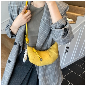 Detail of yellow crescent bag with knotted shoulder strap and spotted plush pendant