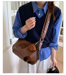 Close-up of brown textured leather dumpling bag with wide shoulder strap and bear charm