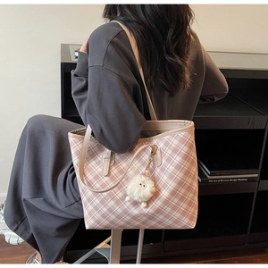 Detail of pink plaid tote bag with golden logo lettering and white plush ball charm