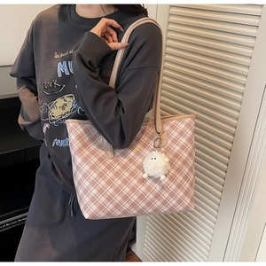 Detail view of pink plaid tote bag with plush ball charm worn by a model in casual style