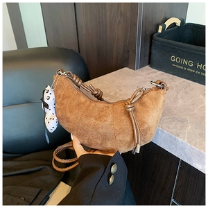 Detail of brown suede crescent bag featuring quilted texture and knotted strap with doll
