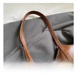 Detailed macro view of the slim brown PU leather handles and fine stitching on the tote bag