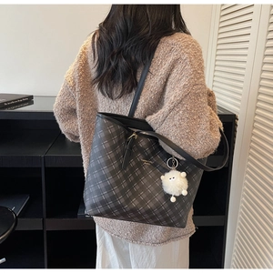 Detail of checkered tote bag featuring black leather straps and a white plush lamb charm