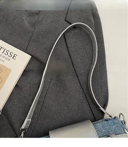 Close-up of smooth gray leather shoulder strap with silver metal buckle on a denim handbag