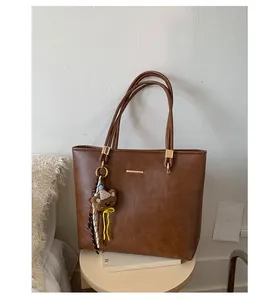 Detail of a brown large capacity tote bag with golden plaque and a cute bear keychain
