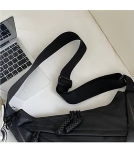 Detail of adjustable wide shoulder strap and woven zipper pull on black nylon crossbody bag