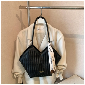Detail of black woven tote bag with V-shaped opening, gold metal logo, and decorative silk scarf
