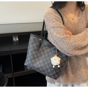 Detail of grey checkered tote bag with gold logo and white sheep plush charm pendant