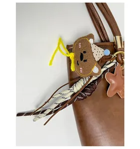 Detail of plush bear keychain with woven ropes and leather star on a brown tote bag