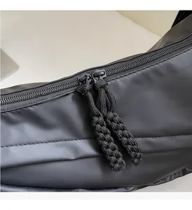 Detail of dual metal zippers with black woven rope pulls on a matte crossbody bag