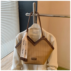 Detailed shot of checkered woven straw tote bag with brown leather trim and hanging ribbon