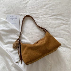 Detail of a brown suede baguette bag featuring a cute plush bear charm on the strap